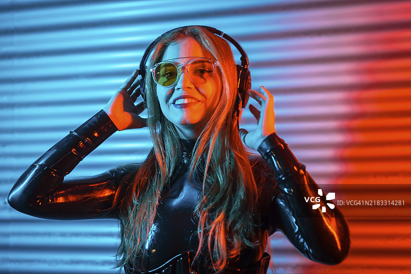 一位金发快乐的女性在霓虹灯闪烁的城市空间中佩戴耳机的肖像图片素材