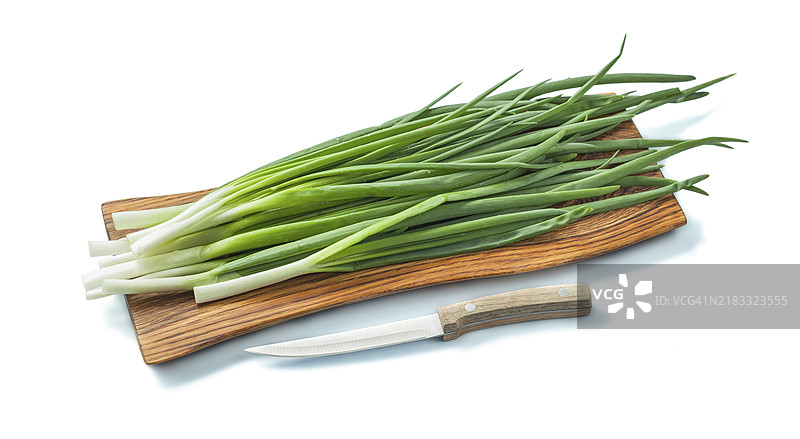 新鲜的青葱茎放在木砧板上，旁边有一把厨房刀。图片素材