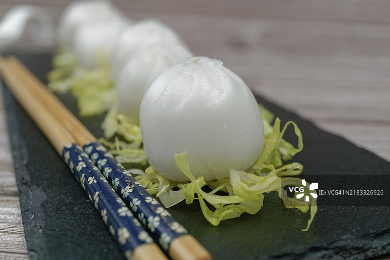 虾仁小笼包放在生菜上，搭配石板盘、筷子和陶瓷勺，旁边有酱油。图片素材