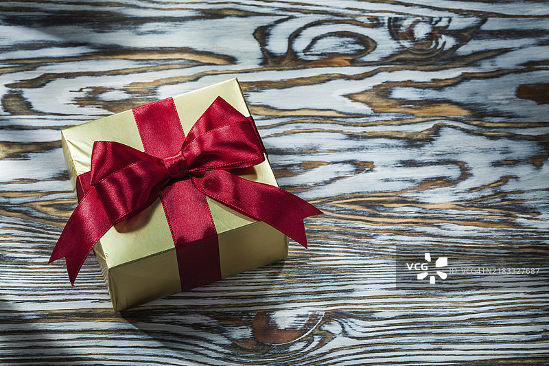 木板上的金色礼品盒，系着红色结图片素材
