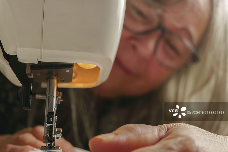 模糊的白发老妇人在缝纫机上缝制白色布料图片素材