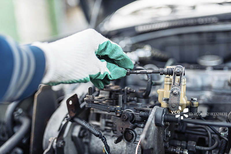 汽车修理工通过油门线杆调节燃油供应，设置怠速。图片素材