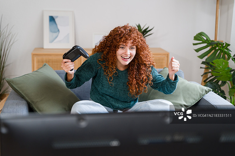 兴奋的年轻女性在家沙发上赢得电子游戏胜利图片素材
