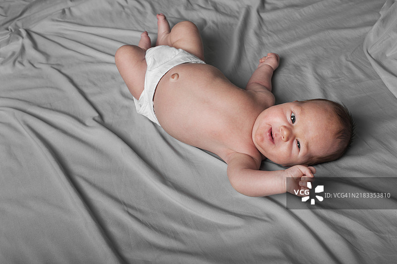 穿着尿布的新生儿躺在灰色床单上图片素材