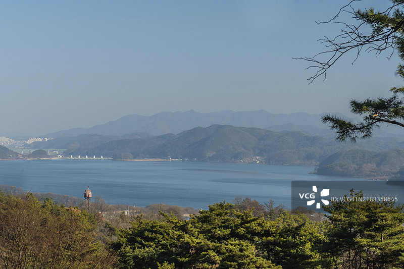 阴霾多云天的水库风景，背景有山脉、城市建筑和白色桥梁。图片素材