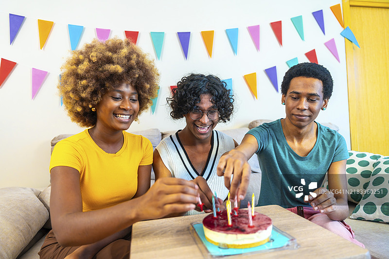 快乐的多元朋友们在家准备生日蛋糕并放置蜡烛图片素材