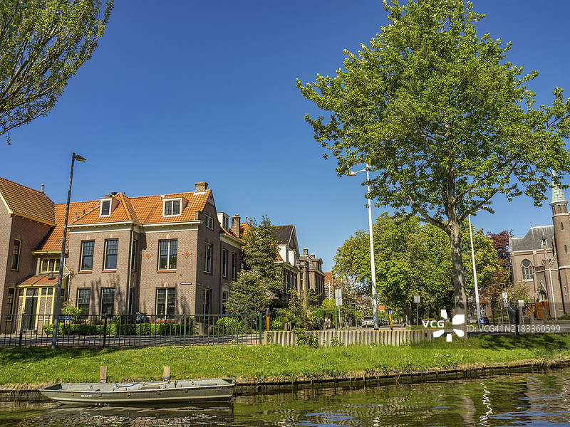 阿尔克马尔，荷兰，清澈的天空下，运河旁的老房子和树木环绕的氛围街道图片素材