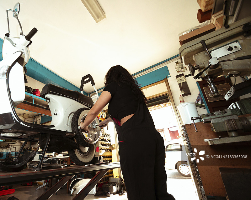 一位专注的女性机械师在车间里修理滑板车的轮胎，展现了拉丁裔女性在传统男性职业中的力量，体现了现实生活中的女性力量。图片素材