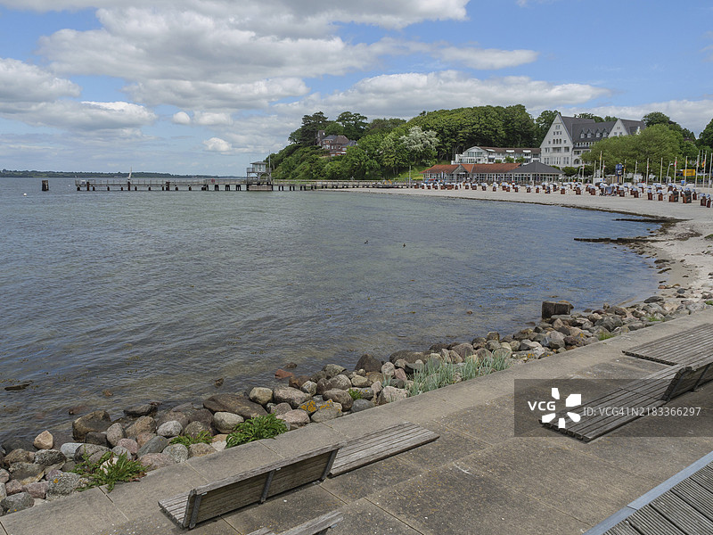 德国石勒苏益格-荷尔斯泰因州格吕克斯堡的海滩沿岸步道，设有长椅、卵石和多云的天空。图片素材