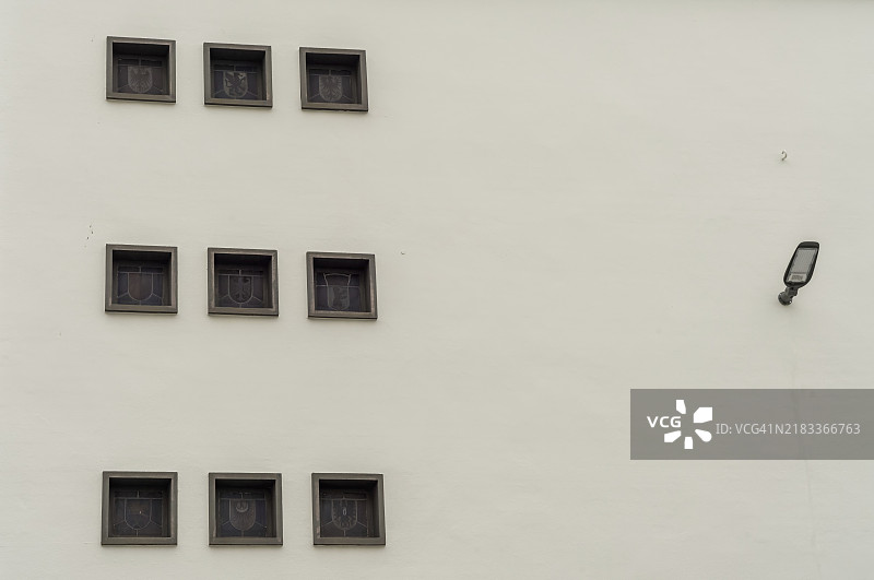 九个方形窗户装饰在一面白色墙壁上，右侧有一盏灯。图片素材