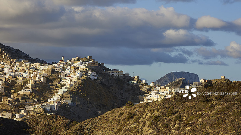 一个村庄坐落在山上，背景是浓密的云朵和蓝天，色彩斑斓的山村，晨光，奥林波斯，卡尔帕索斯，多德卡尼斯，希腊群岛，希腊，欧洲图片素材