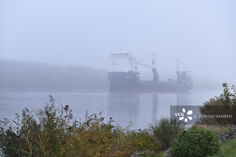 在德国施莱斯维希-霍尔斯坦的基尔运河中，货船在雾中航行图片素材
