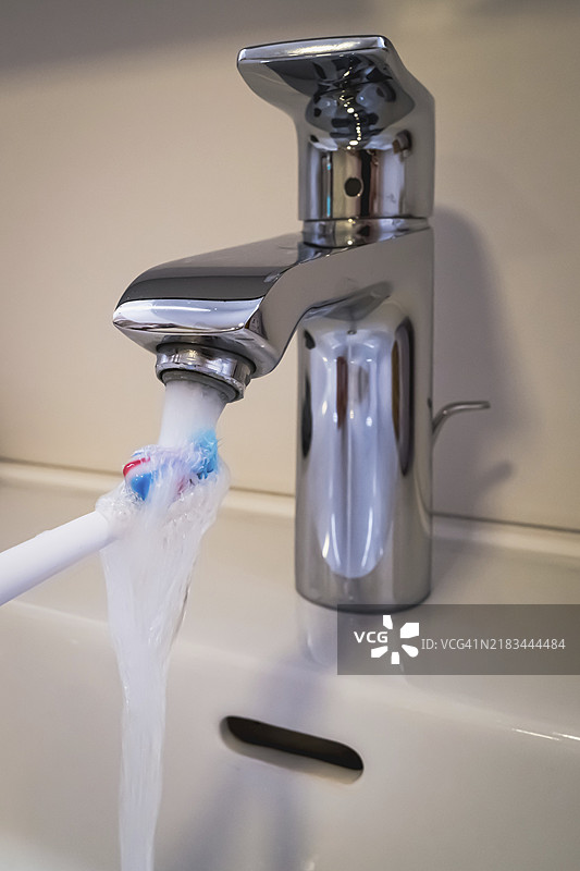 一只浴室水龙头在流动，牙刷在水下，象征着水的消耗。图片素材