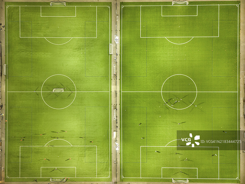 从鸟瞰图看，两片对称的足球场，绿色场地上散落着球员。图片素材