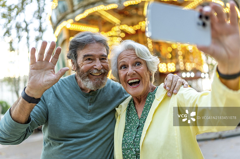 老年夫妇在城市的旋转木马上自拍并向镜头挥手图片素材