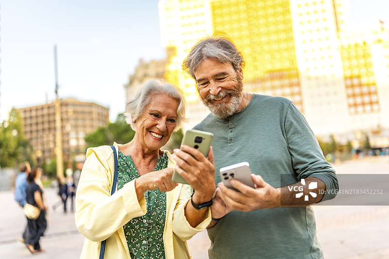 现代可爱的老年夫妇在城市中开心地使用智能手机的正面肖像图片素材
