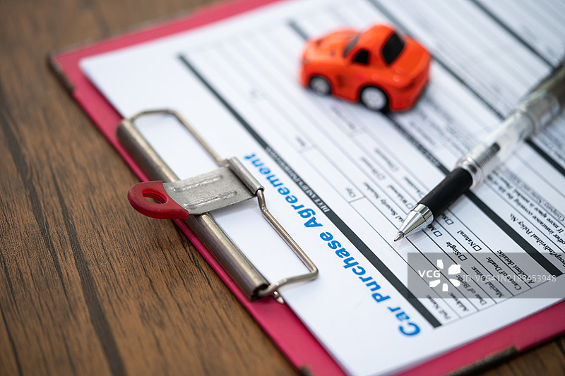 经纪代理与玩具车，手持签署的购销合同和抵押贷款文件，包括意外保险。图片素材