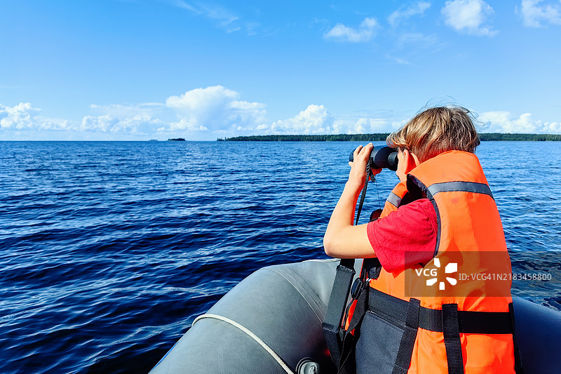 年轻的探险者穿着橙色救生衣，手持望远镜在平静的湖面上扫描地平线图片素材