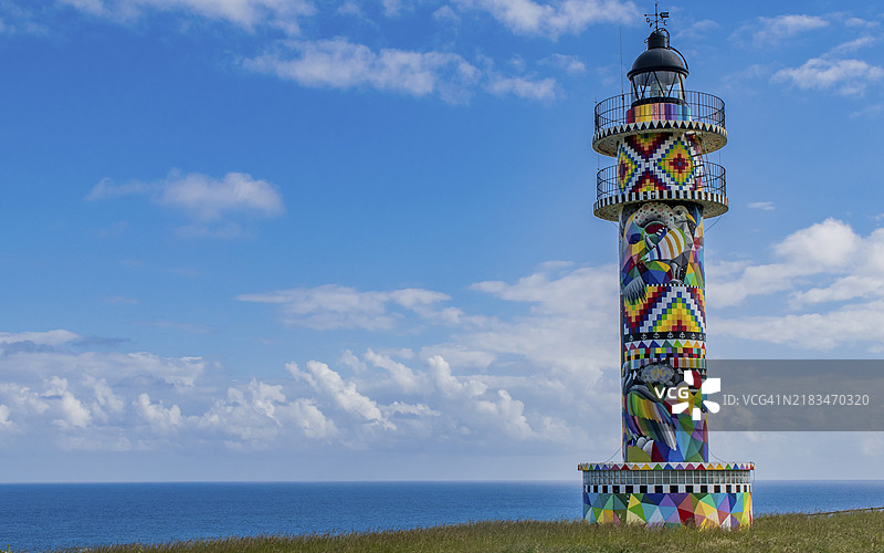 一座色彩鲜艳的灯塔矗立在蓝天与海洋之间，前景是一座草坡，阿霍灯塔，颜色，坎塔布里亚，西班牙，欧洲图片素材