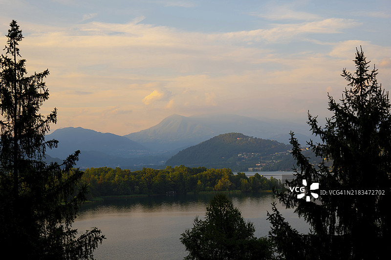 瑞士提契诺州卡斯拉诺的卢加诺湖和山脉的全景，蓝天白云下的日落景色图片素材