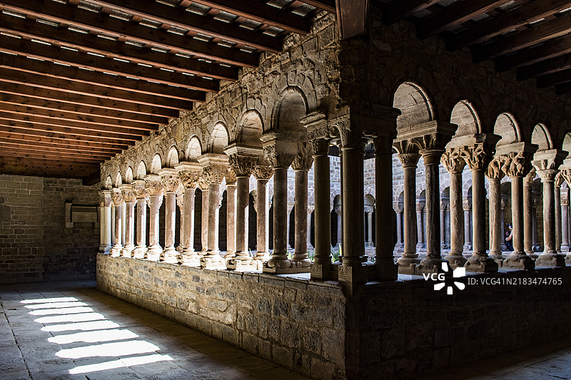 阳光照耀的中世纪回廊，石拱和柱子营造出宁静的氛围，位于西班牙加泰罗尼亚的斯塔·玛丽亚·德斯塔尼，罗曼式回廊。图片素材