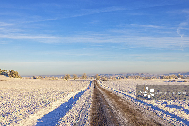 美丽的冬季乡村风景中，长长的笔直乡村道路上覆盖着冰雪，远处的地平线尽收眼底，瑞典，欧洲图片素材