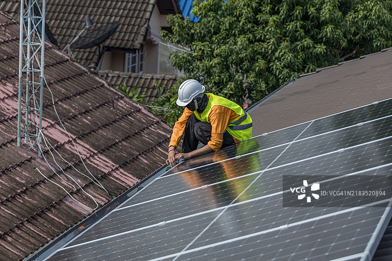 技术人员在房屋屋顶上安装光伏太阳能模块。工程师在房屋屋顶上安装或修理太阳能电池。技术工人在太阳能面板上工作。太阳能面板技术人员在房屋屋顶上工作。图片素材