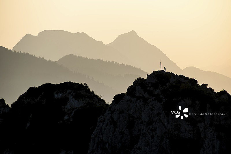 孤独的登山者在德国巴伐利亚的基门高阿尔卑斯山的霍恩德尔万德峰顶，清晨的光线下，兹维泽尔山和霍赫斯陶芬山的轮廓映衬其间。图片素材