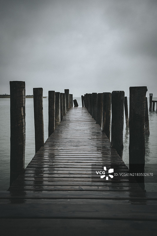 一座长长的木栈桥通向雾气弥漫的水面，周围环绕着宁静的氛围，位于奥地利布尔根兰州的波德斯多夫。图片素材