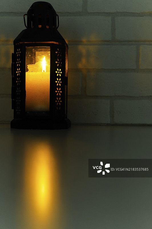 带有点燃蜡烛的灯，光线在桌子和砖墙上反射图片素材