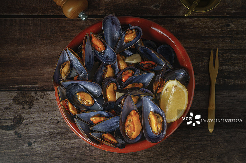 陶锅中的蒸贻贝配柠檬，旁边有金属研钵和胡椒瓶图片素材