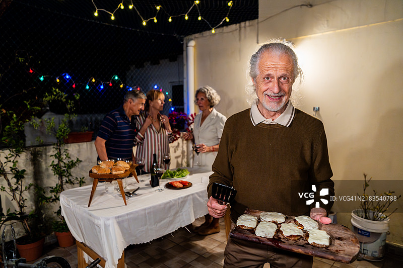 一位老年男子在家庭聚会上手持切菜板和汉堡的肖像图片素材
