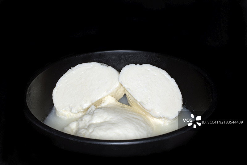 自制切片马苏里拉奶酪躺在乳清中，黑色背景的摄影作品图片素材