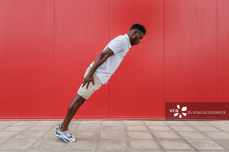 男子在阳光明媚的户外，明亮的红墙前向前走。图片素材