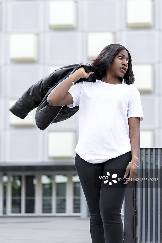 简单而时尚：一位年轻黑人女性的肖像，穿着简约的白色T恤和黑色裤子，背景是一座时尚现代的建筑。图片素材
