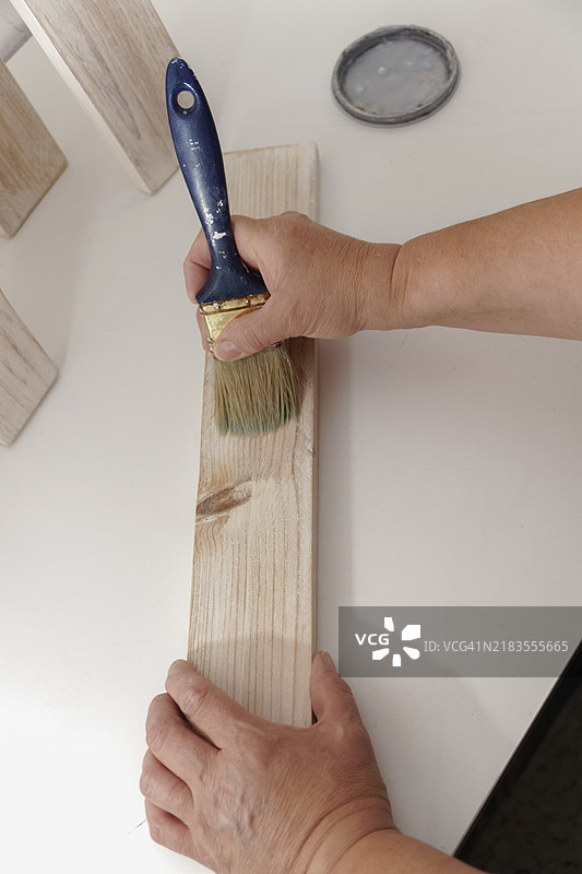 女人的手用画笔在木板上涂白色。图片素材