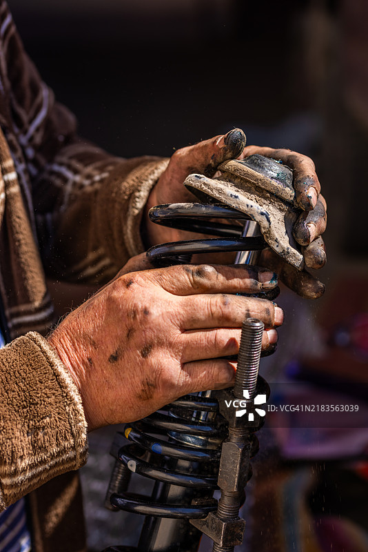 一位机械师在进行DIY汽车修理时，正在组装压缩螺旋弹簧，手上布满老茧。图片素材