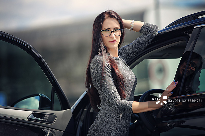 一名女性侧身站在打开的车门旁，立陶宛考纳斯地区市。图片素材