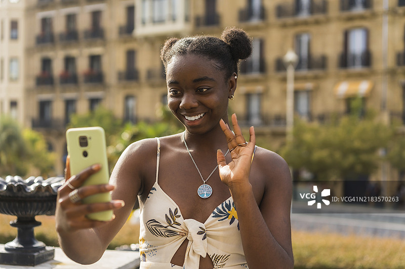 年轻可爱的非洲女性在街上用手机进行视频通话时挥手。图片素材