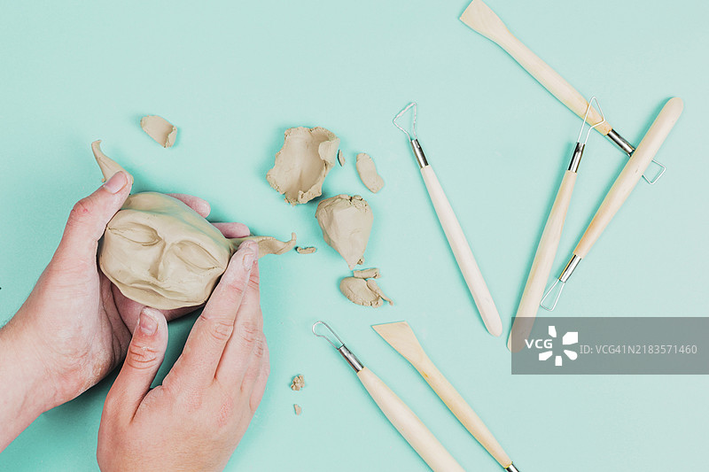 雕塑家特写，正在用粘土创作雕像面孔，背景为彩色。图片素材