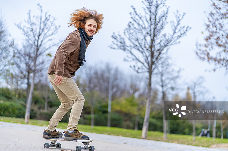 在城市公园里，骑滑板的卷发红发少年图片素材
