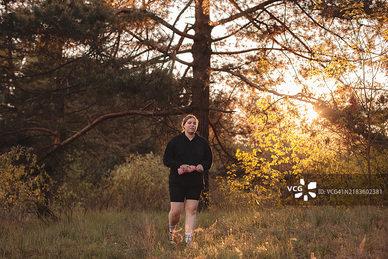 年轻女性在森林中走路，手里拿着水瓶图片素材