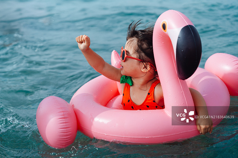 亚洲小女孩在热带海洋中与粉色充气火烈鸟一起游泳，享受夏季假期图片素材