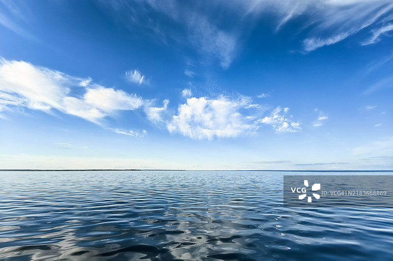宁静的日子里，广阔的湖面在晴朗的蓝天和柔和的白云下。图片素材