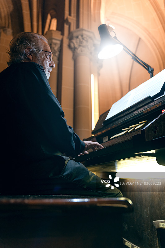 一位专注的老年风琴师在仔细跟随乐谱的同时演奏风琴图片素材