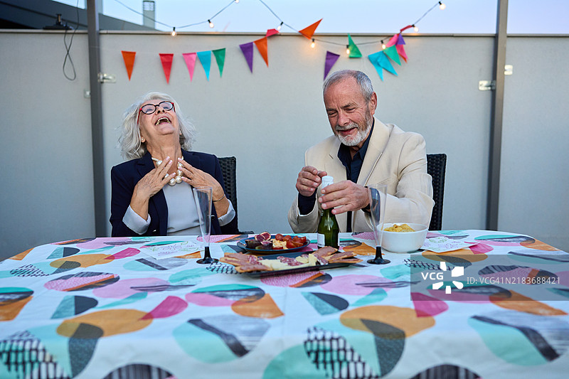 优雅的老年夫妇在屋顶露台派对上欢笑并享用香槟图片素材
