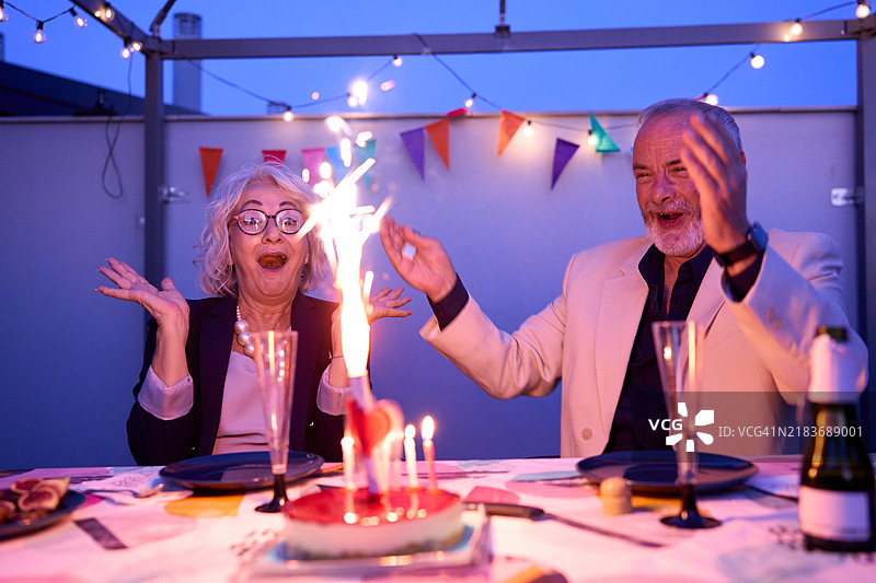 老年夫妇在屋顶露台上庆祝生日，享受烟花和蛋糕图片素材