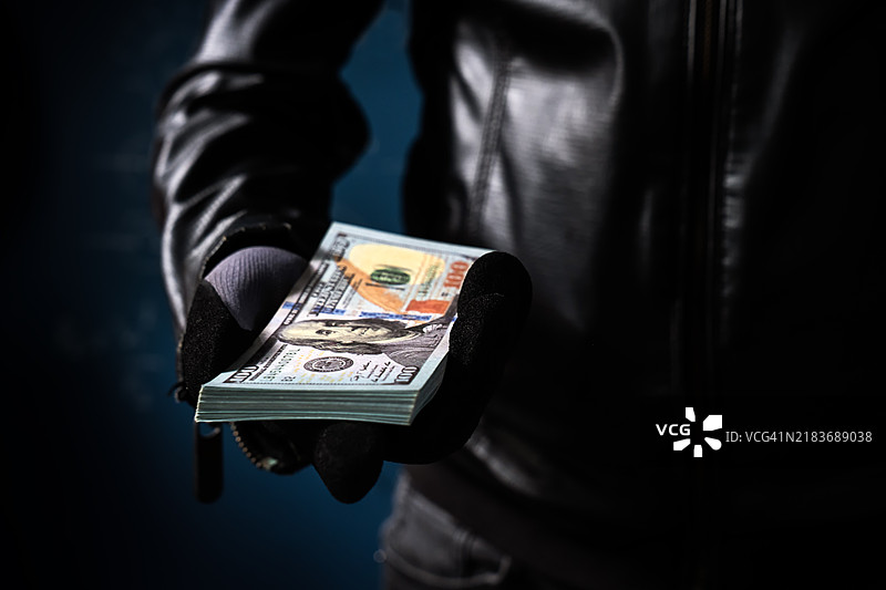 腐败概念。男人手持美元钞票，黑色背景，特写，骗子。图片素材