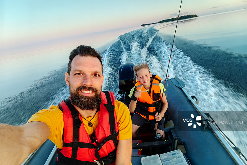 父亲和儿子在宁静的湖面上享受日落时分的高速船之旅图片素材