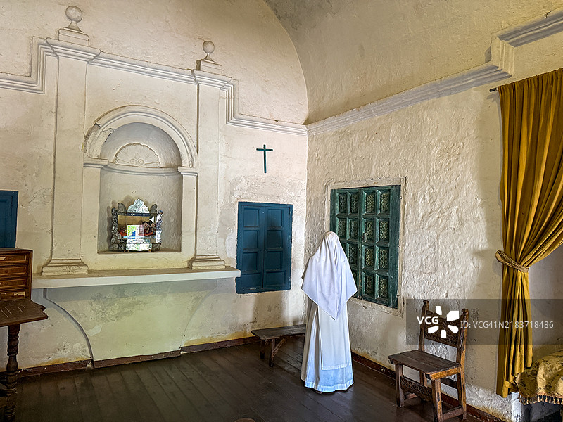 身穿白色习惯的修女雕像背对着房间里的十字架。图片素材